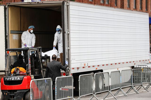 Two men stand in a temporary morgue truck to accept a body.